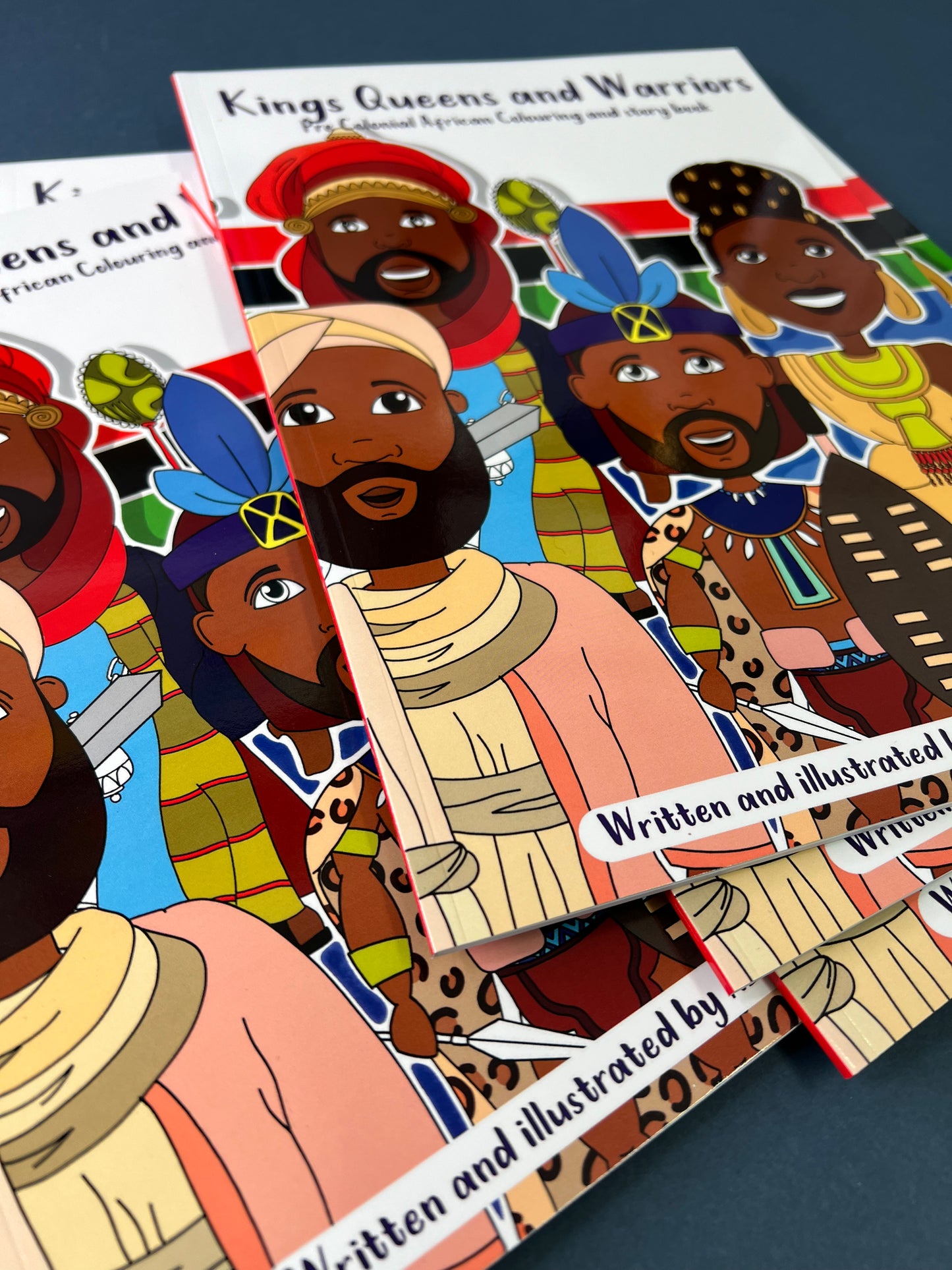 Coloring book titled 'Kings, Queens and Warriors' with illustrations of historical figures on a dark surface.